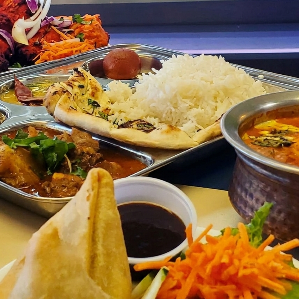 Colorful Indian meal spread with naan, basmati rice, curries, roasted vegetables, samosas, chutneys, and grated carrots.